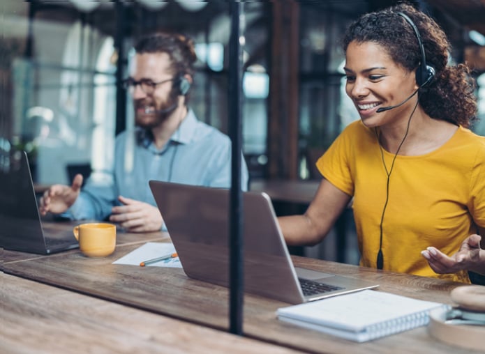 Man and woman seated side by side on laptops and using headsets to provide customer service